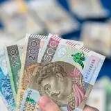 Dłoń trzyma wachlarz polskich banknotów: 50, 100, 200 i 500 zł. To dowód, że można być aktywnie w domu dla każdego, kto oszczędza.