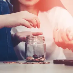 Dwie osoby wrzucają monety do słoika. Zastanawiają się, czy ich dochód mieści się w progu dla funduszu alimentacyjnego.