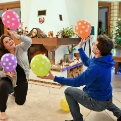 Wesołe zabawy dla 3 osób w domu przy choince. Dwoje ludzi łapie kolorowe balony w kropki, tworząc radosną atmosferę.