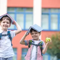 Dwóch chłopców z plecakami i jabłkami w rękach, z książkami na głowach, radośnie wita nowy dzień, kiedy dzieci idą do szkoły.