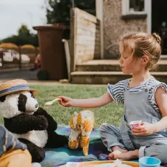 Dziewczynka karmi pluszową pandę na pikniku. Wspaniałe zabawy dla 2 osób na trawie.
