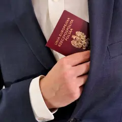 Dłoń wsuwa polski paszport do kieszeni marynarki. Dokument potwierdza, że osoba posiada obywatelstwo.