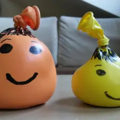 Dwa balony z namalowanymi buźkami, jeden pomarańczowy, drugi żółty. Prosty sposób, jak zrobić gniotka z mąki i wody.