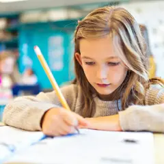 Dziewczynka pilnie pisze w zeszycie, ucząc się do którego roku jest obowiązek szkolny.