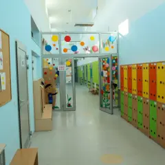 Kolorowy korytarz przedszkola, idealny na wakacje w przedszkolu. Szafki w tęczowych barwach, tablica z liśćmi i rysunki dzieci.