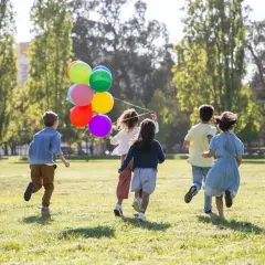 Dzieci biegną po trawie z kolorowymi balonami. Wspaniałe zabawy dla dzieci na dworze w słoneczny dzień.