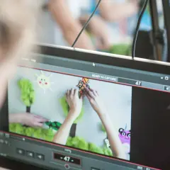 Tworzenie animacji poklatkowej: ręce układają elementy scenografii, słońce i drzewa, gotowe do ujęcia.