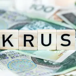Litery K, R, U, S na tle polskich banknotów. Symbolizuje to świadczenie uzupełniające KRUS, wsparcie dla rolników.