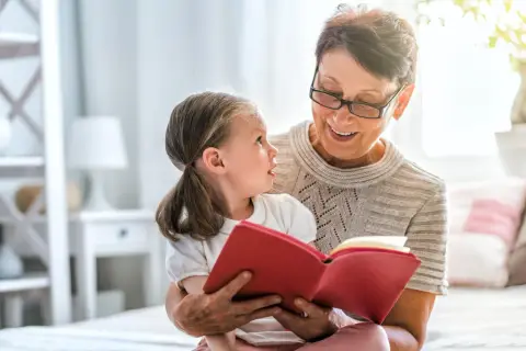 Uśmiechnięta opiekunka prawna czyta książkę małej dziewczynce.