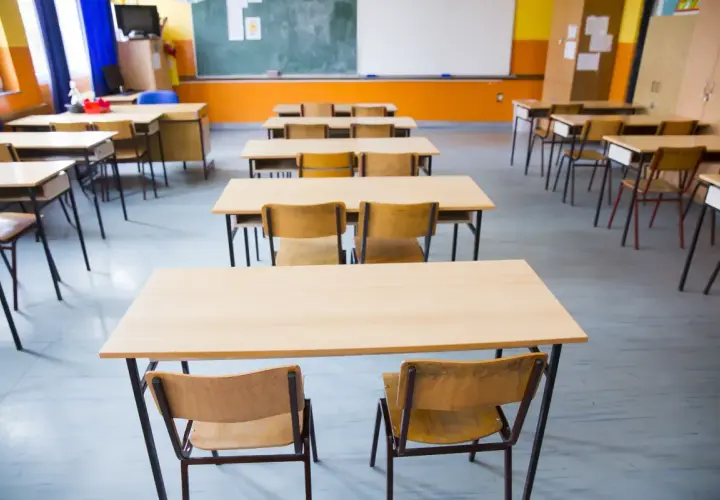Puste ławki i krzesła w sali lekcyjnej czekają na uczniów. Obowiązek szkolny wkrótce wypełni te miejsca śmiechem i nauką.