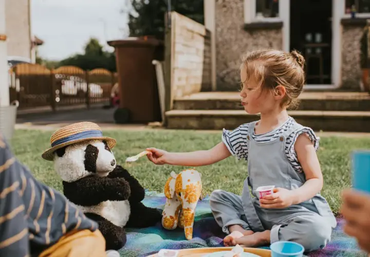Dziewczynka karmi pluszową pandę na pikniku. Wspaniałe zabawy dla 2 osób na trawie.