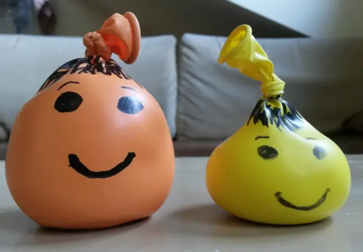 Dwa balony z namalowanymi buźkami, jeden pomarańczowy, drugi żółty. Prosty sposób, jak zrobić gniotka z mąki i wody.