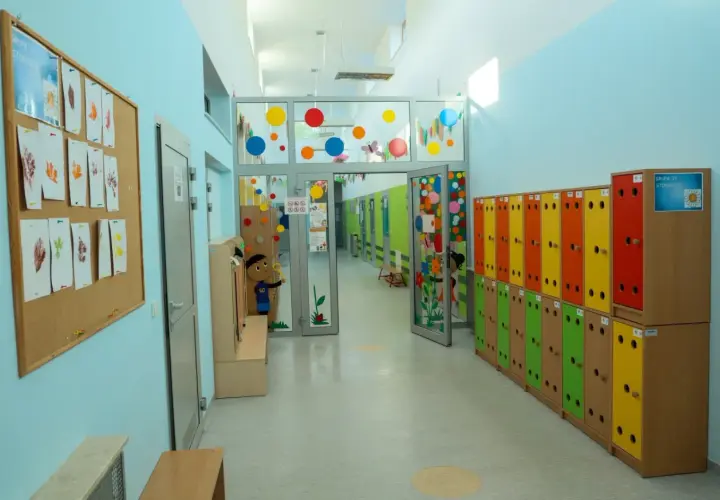 Kolorowy korytarz przedszkola, idealny na wakacje w przedszkolu. Szafki w tęczowych barwach, tablica z liśćmi i rysunki dzieci.