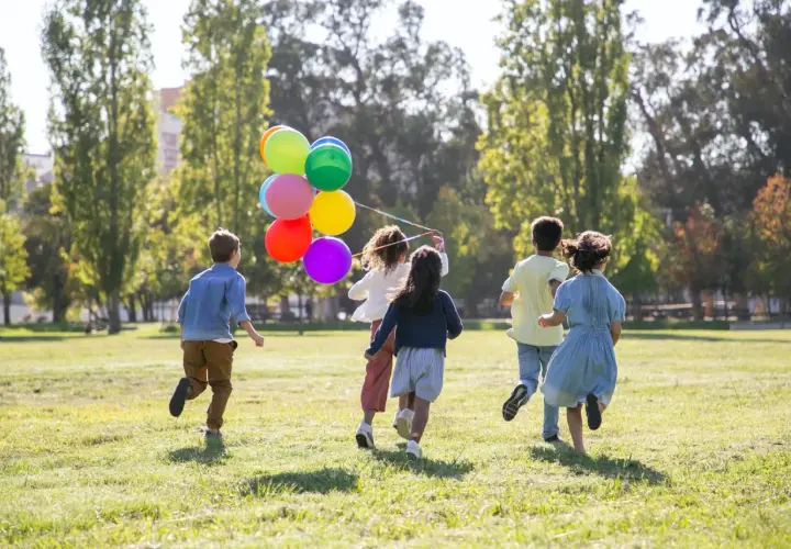 Dzieci biegną po trawie z kolorowymi balonami. Wspaniałe zabawy dla dzieci na dworze w słoneczny dzień.