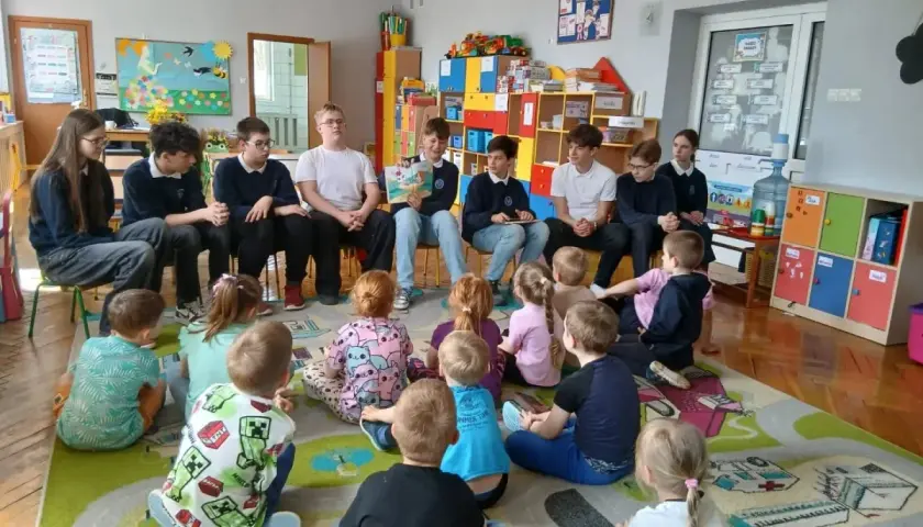 Młodzież czyta dzieciom w przedszkolu. Wspaniały przykład wolontariatu w przedszkolu, budujący relacje i rozwijający wyobraźnię najmłodszych.