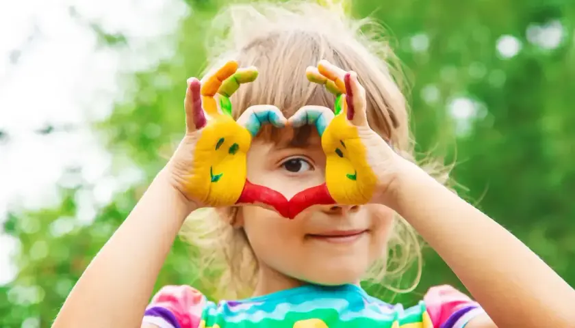 Radosne zabawy dla 4 latka! Dziecko maluje ręce farbami, tworząc serce i uśmiechnięte buźki.
