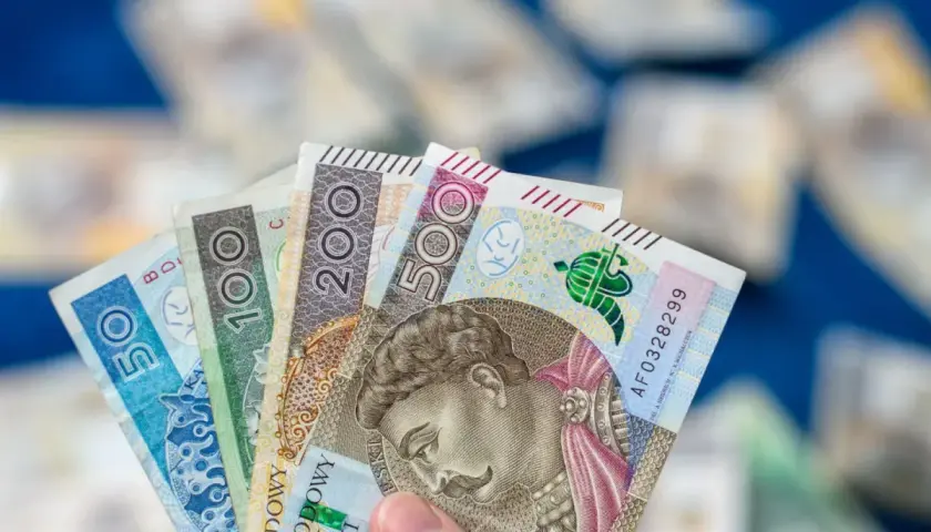Dłoń trzyma wachlarz polskich banknotów: 50, 100, 200 i 500 zł. To dowód, że można być aktywnie w domu dla każdego, kto oszczędza.