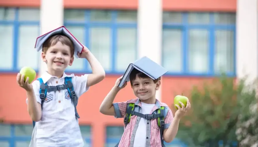 Dwóch chłopców z plecakami i jabłkami w rękach, z książkami na głowach, radośnie wita nowy dzień, kiedy dzieci idą do szkoły.