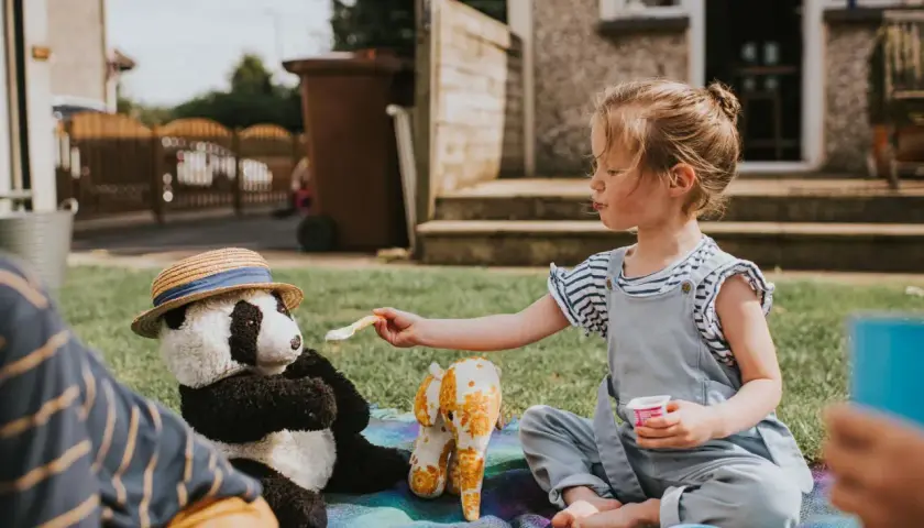 Dziewczynka karmi pluszową pandę na pikniku. Wspaniałe zabawy dla 2 osób na trawie.