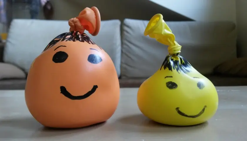 Dwa balony z namalowanymi buźkami, jeden pomarańczowy, drugi żółty. Prosty sposób, jak zrobić gniotka z mąki i wody.
