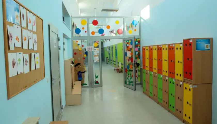 Kolorowy korytarz przedszkola, idealny na wakacje w przedszkolu. Szafki w tęczowych barwach, tablica z liśćmi i rysunki dzieci.