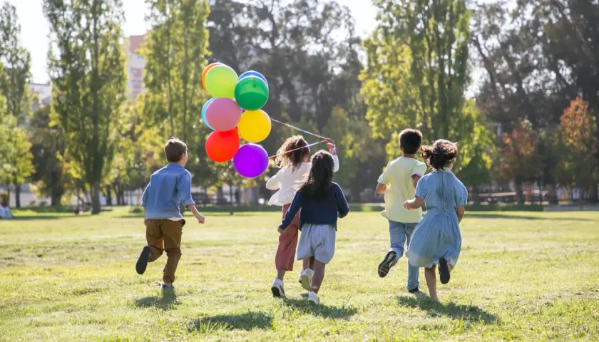 Dzieci biegną po trawie z kolorowymi balonami. Wspaniałe zabawy dla dzieci na dworze w słoneczny dzień.