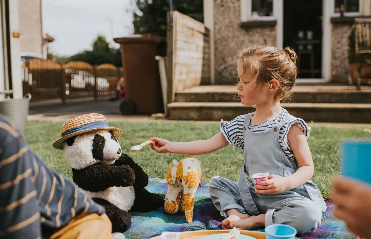 Dziewczynka karmi pluszową pandę na pikniku. Wspaniałe zabawy dla 2 osób na trawie.