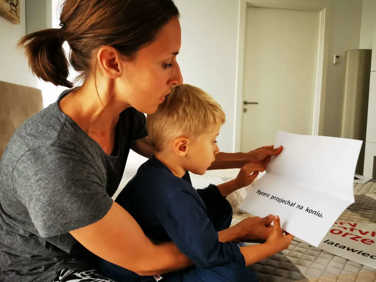 Mama pomaga 8-latkowi nauczyć się czytać, wspólnie czytają tekst "Rycerz przyjechał na koniu".