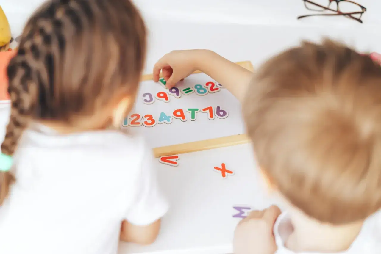 Dzieci układają kolorowe cyferki i znaki na tablicy, bawiąc się matematyką.