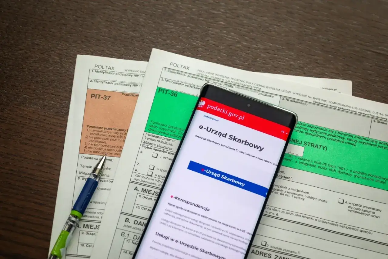 Formularze PIT, smartfon z aplikacją e-Urząd Skarbowy i długopis.