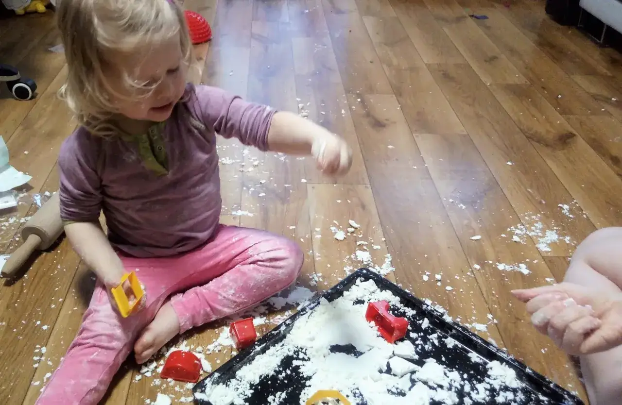 Mała dziewczynka bawi się na podłodze, rozsypując sztuczny śnieg i czerwone foremki.
